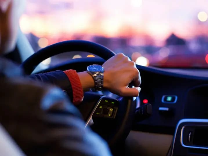 Hands on steering wheel at dusk